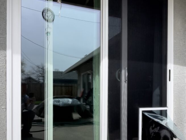 White sliding glass door with built-in pet door and screen for dogs on residential patio